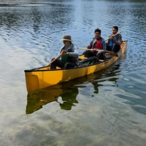 Three scouts paddling a yellow canoe across a calm lake